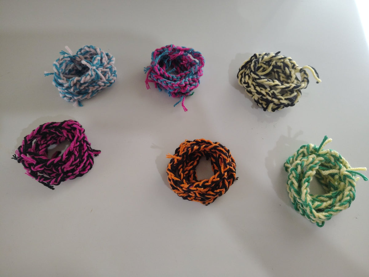 Six handmade braided yarn bracelets in blue/white, pink/blue, black/cream, pink/black, orange/black, and green/cream
